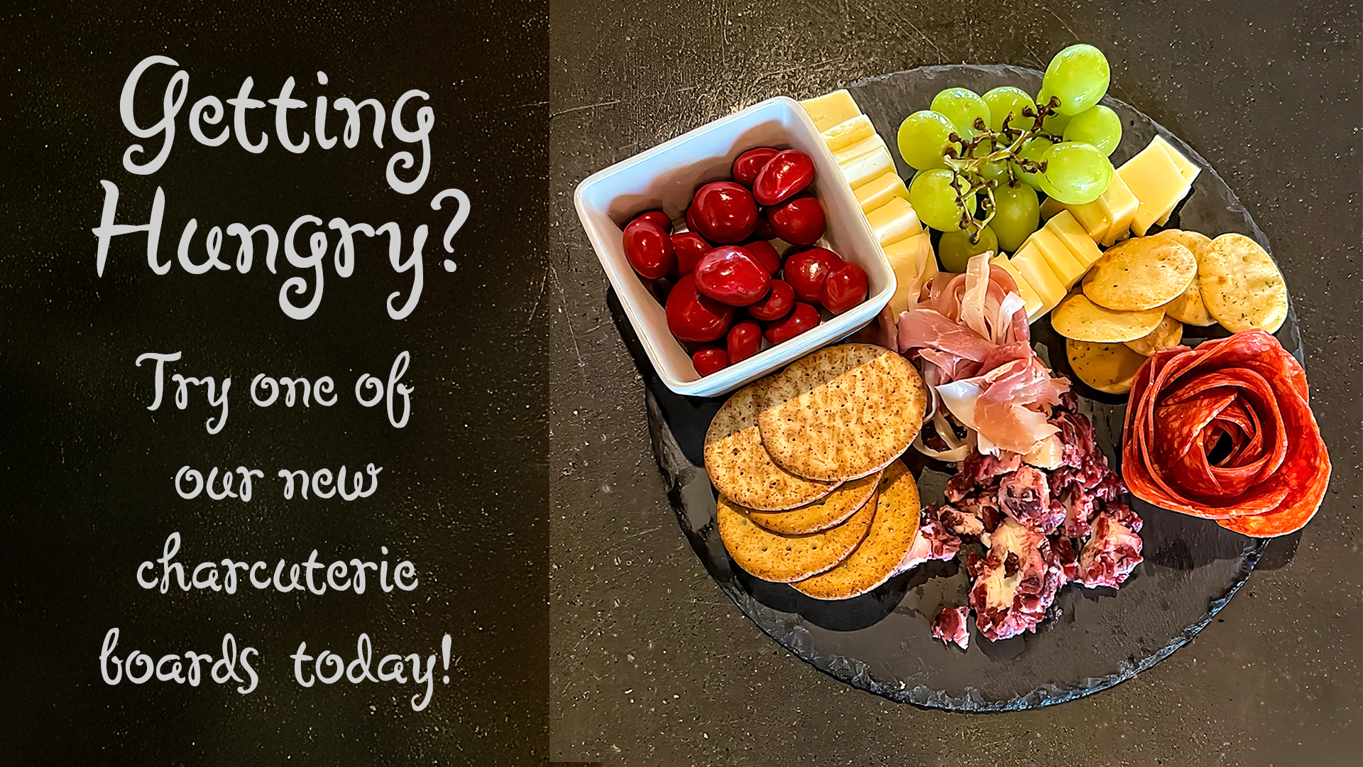 A charcuterie board featuring grapes, cheese, crackers, and sliced meats arranged on a slate platter.