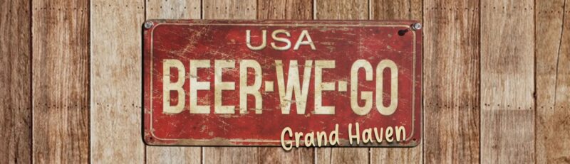 A vintage-style sign that reads 'Beer We Go' with 'Grand Haven' below it, set against a wooden background.