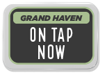 Sign displaying 'Grand Haven ON TAP NOW' in bold white letters on a dark background.